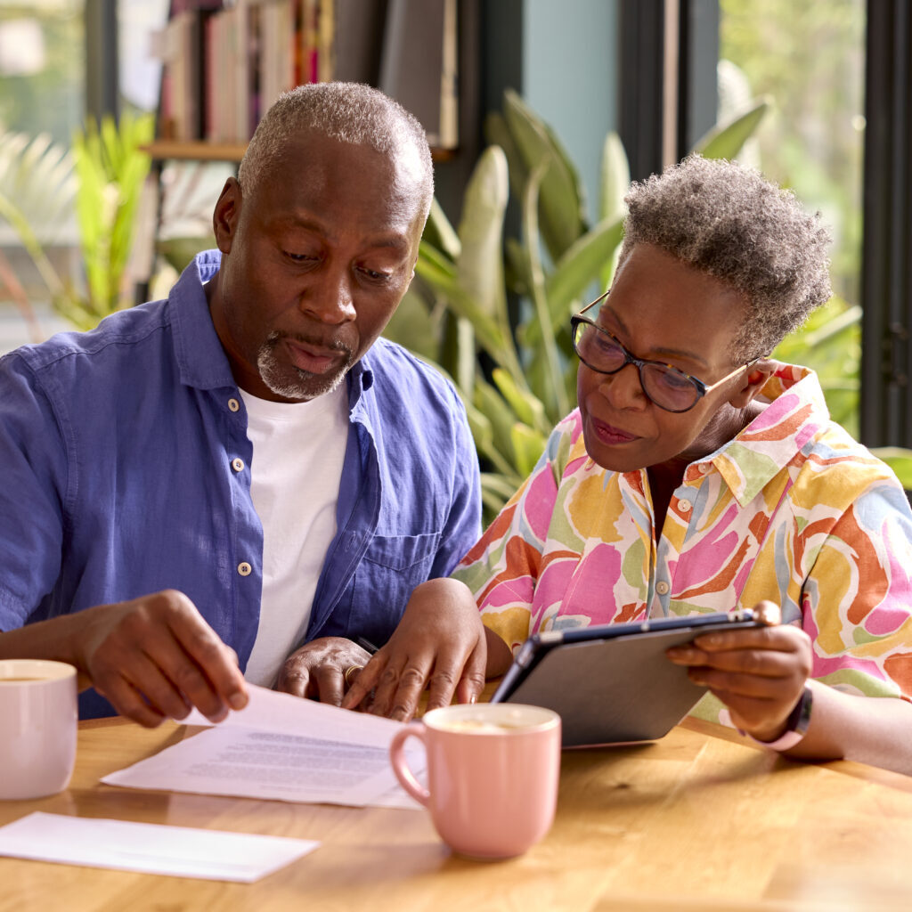 Senior Couple Sitting Around Table At Home Reviewing Finances Using Digital Tablet