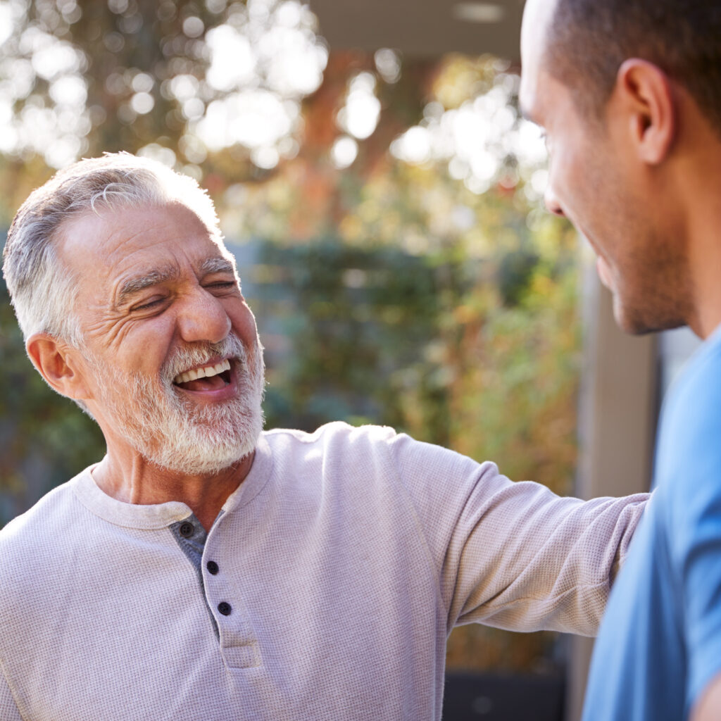 Senior Hispanic Man Talking And Laughing With Adult Son In Garden At Home